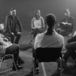 A diverse group of people in a circle discussing and supporting each other in a therapy session.