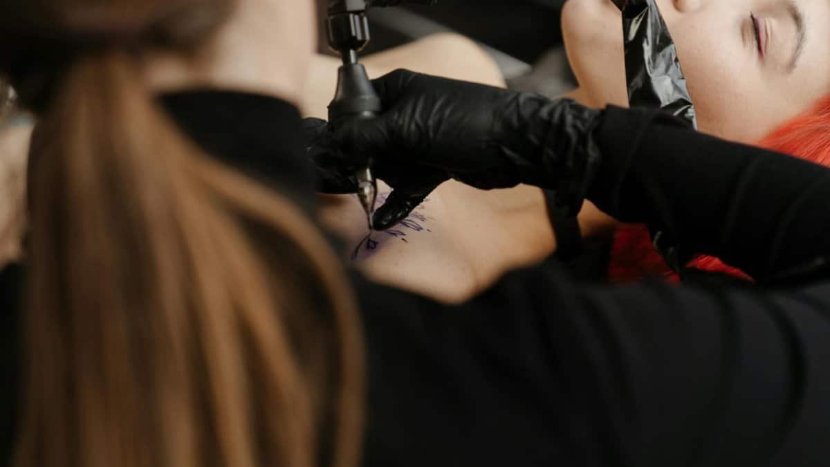 A skilled tattoo artist focuses on creating a design on a client's shoulder in a modern tattoo studio.