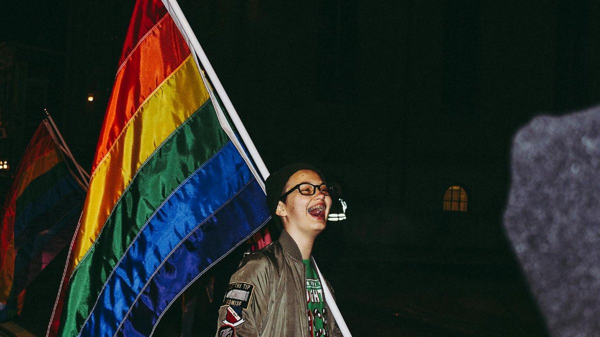 A person celebrates with a colorful pride flag at a nighttime event, expressing joy and freedom.