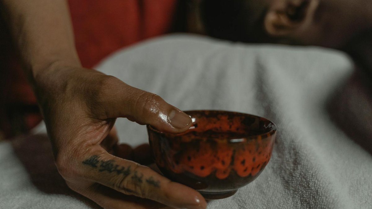 Close-up of a tattooed hand delicately holding a red ceramic bowl, creating a warm and intimate scene.
