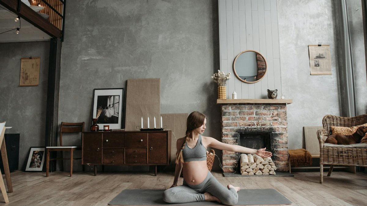 Pregnant woman practicing yoga in a cozy living room with her pet dog nearby.