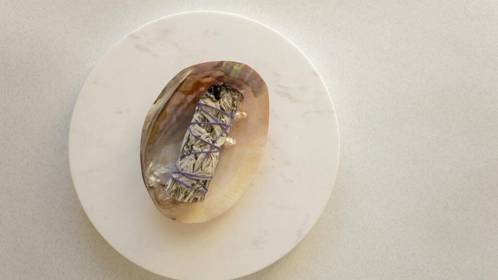 A sage smudge stick on a decorative shell placed on a marble surface, captured from above.