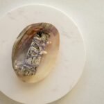 A sage smudge stick on a decorative shell placed on a marble surface, captured from above.