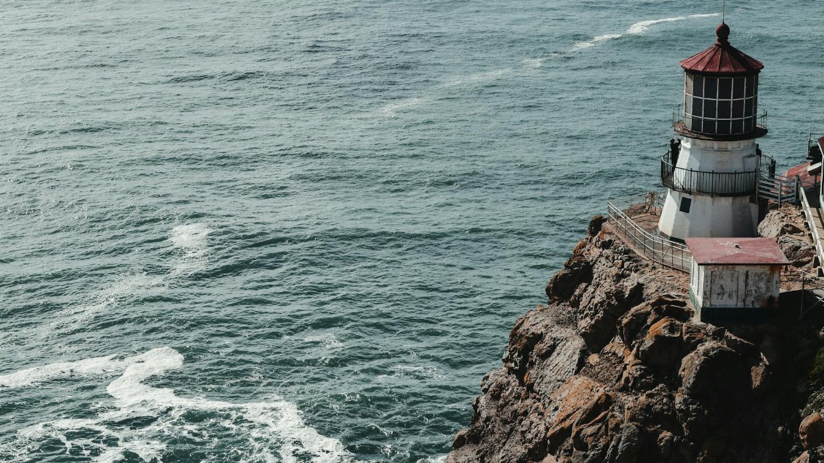 From above of small shabby beacon on top of rocky cliff with waving ocean below