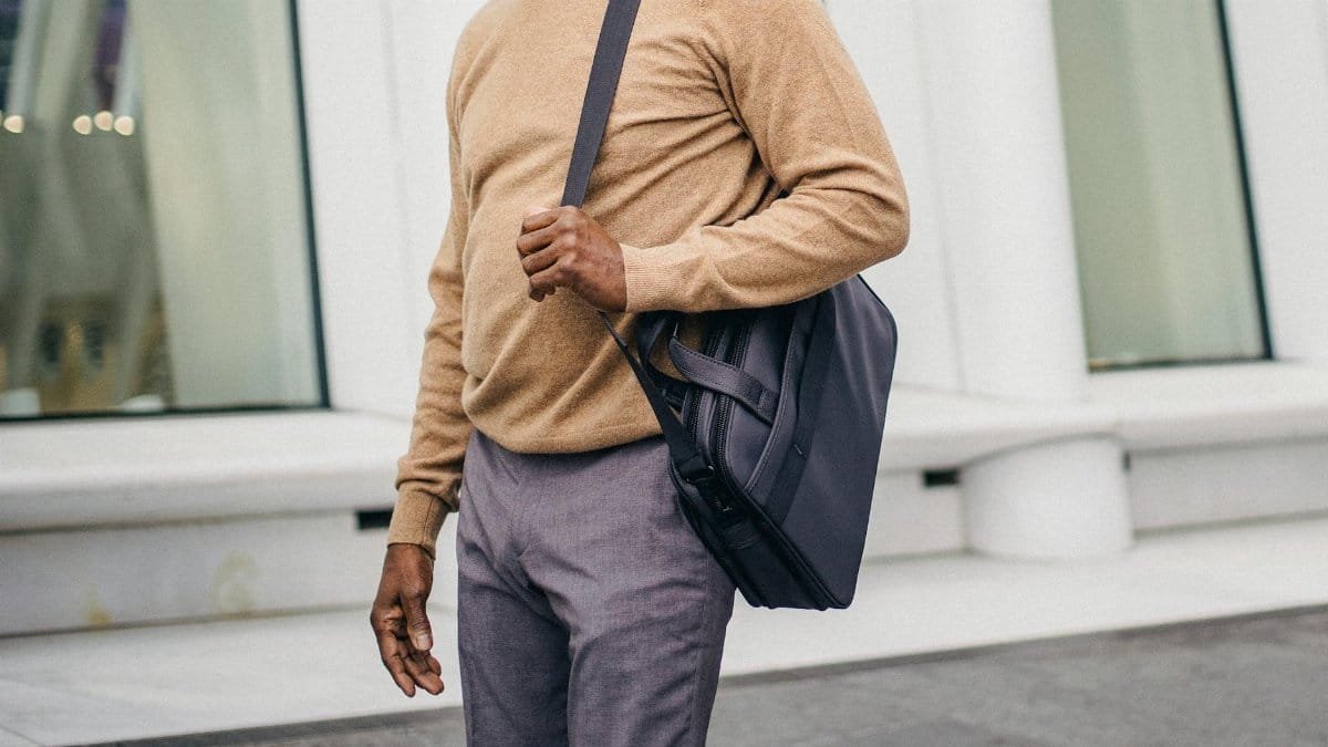 Faceless African American elegant male in jersey and pants carrying case bag on street