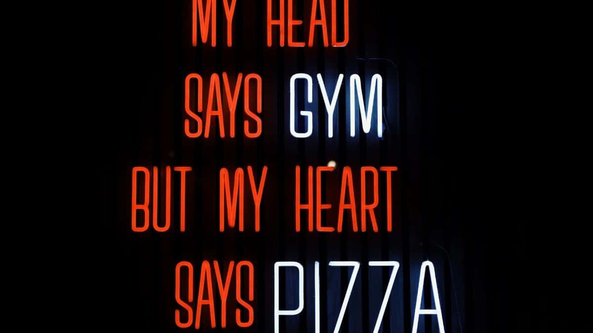Colorful neon sign humorously declares 'My head says gym but my heart says pizza' in Jönköping, Sweden.