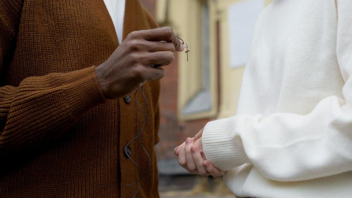 Two individuals exchanging a cross necklace, symbolizing faith and connection.