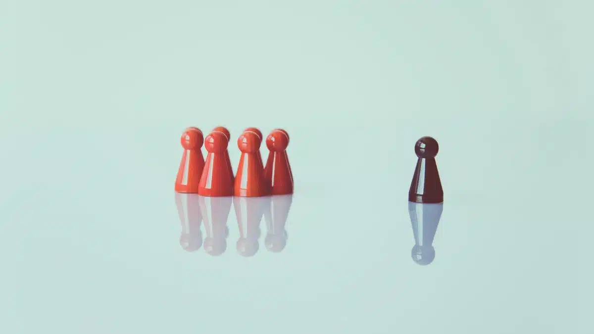 Red game pieces grouped with one isolated piece symbolizing social distancing on a reflective surface.