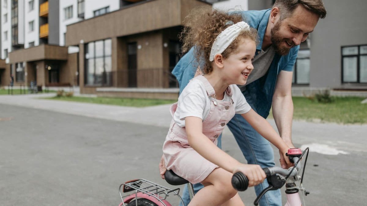 Father helps daughter learn to ride a bike in an urban setting, capturing joy and bonding.