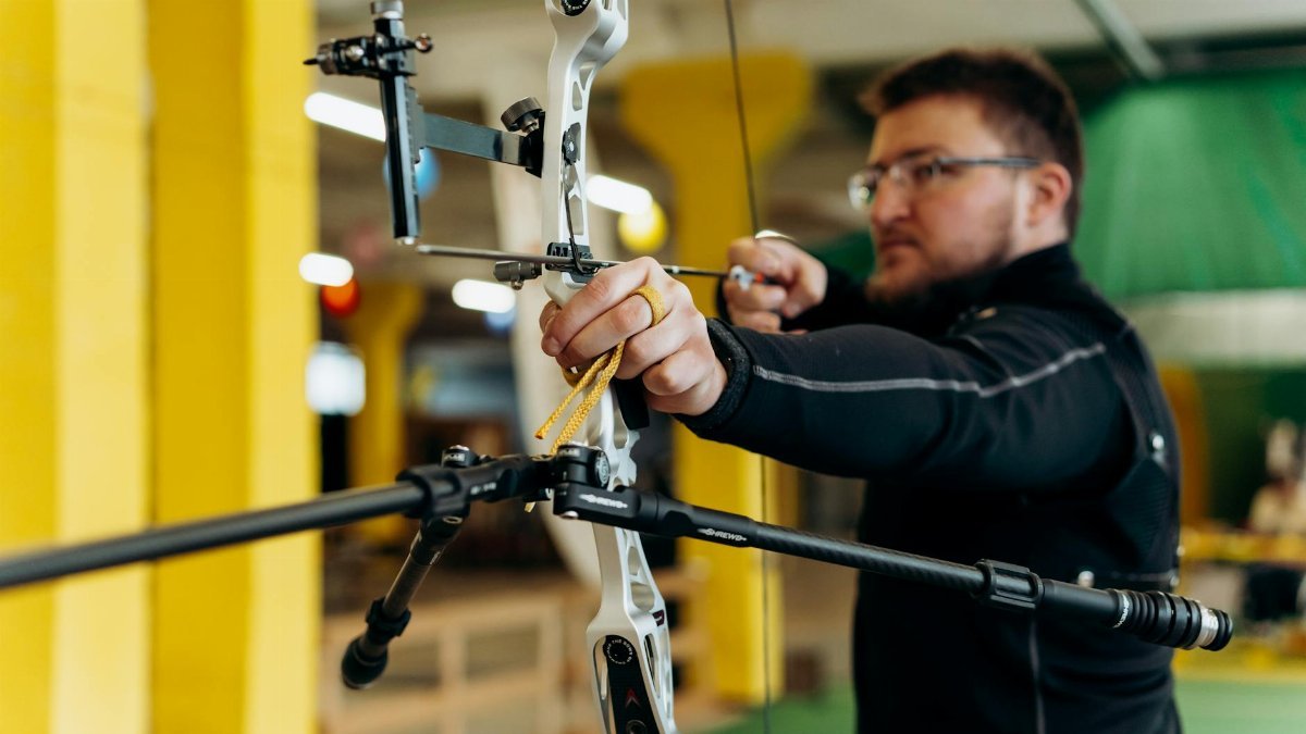 Man concentrating on aiming during an indoor archery practice session.