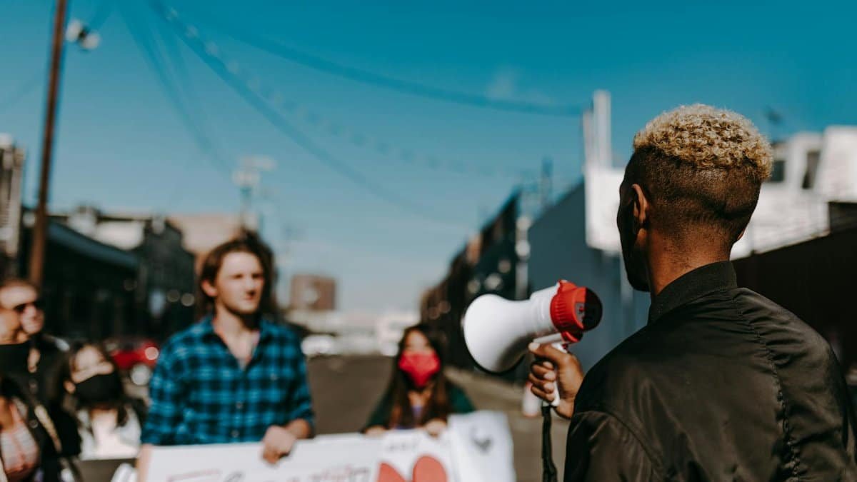 A diverse group of people protesting in an urban setting, with a focus on a speaker using a megaphone.