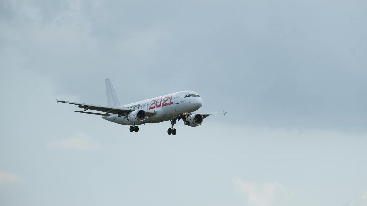 An Airbus A320 airplane with '2021' livery captured in mid-air against a cloudy sky.