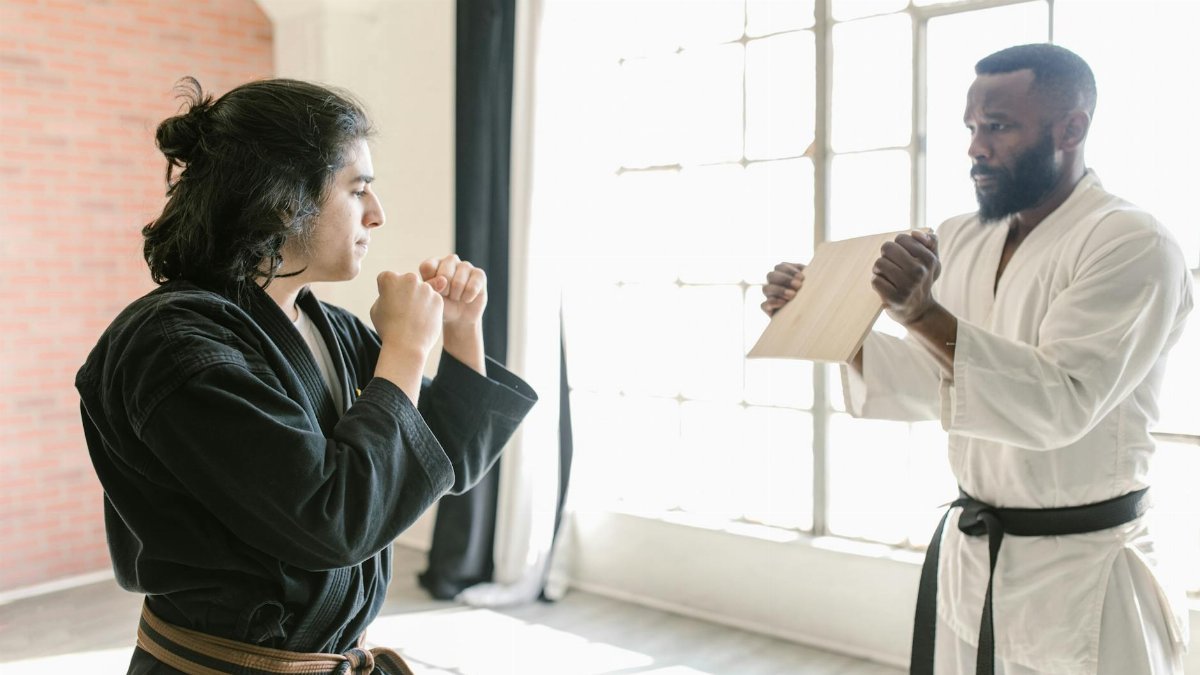 Two martial artists practicing board breaking technique in a sunlit dojo, wearing traditional uniforms.