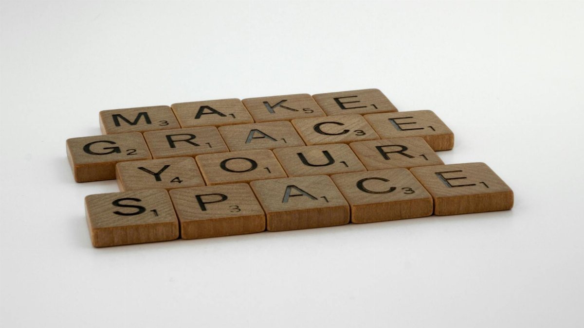 Wooden Scrabble tiles form the message "Make Grace Your Space" on a white surface.