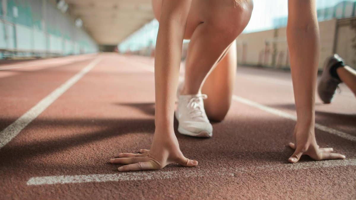 Focused female athlete in crouch start position preparing to sprint on an indoor track.