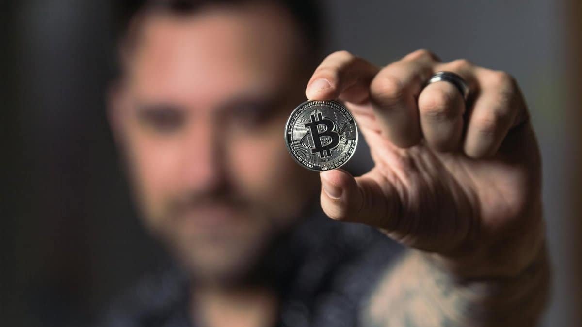 Adult male hand holding a Bitcoin, showcasing cryptocurrency focus indoors.