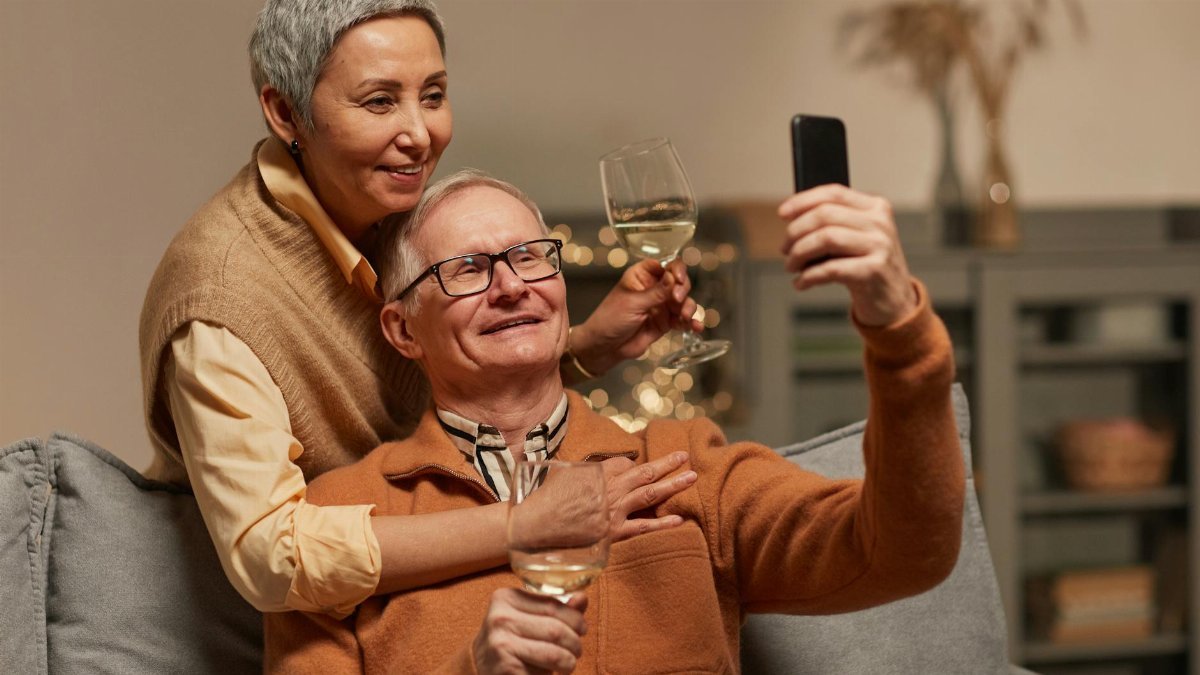 Happy senior couple capturing a memorable moment with a selfie indoors, enjoying wine together.