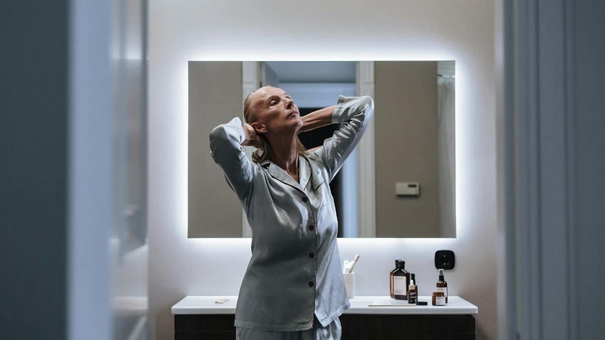 Senior woman enjoying a self-care routine in a modern bathroom, captured in soft evening light.