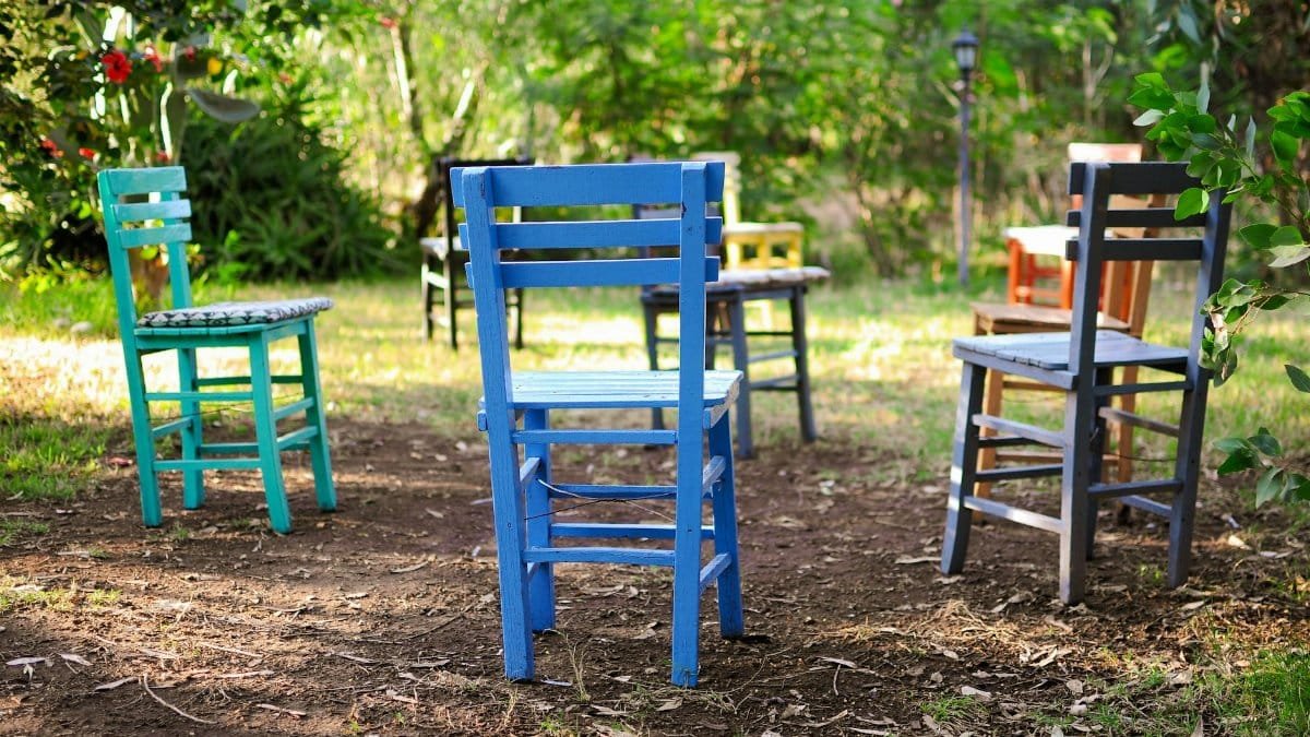 Vibrant wooden chairs arranged in a circle in a lush garden outdoors.