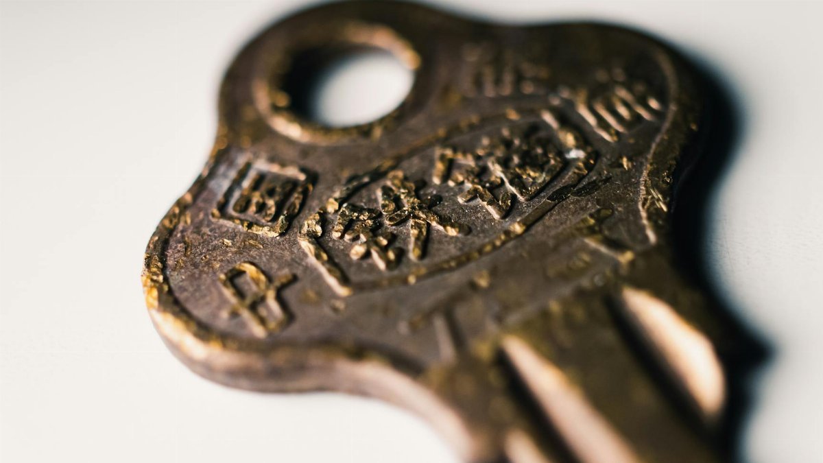 Macro shot of an old brass key featuring worn text on a white surface.