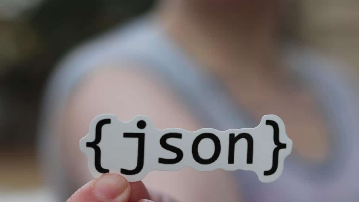 A hand holding a JSON text sticker, symbolic for software development.