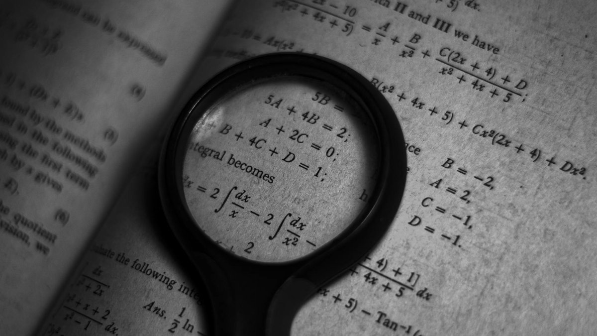 A magnifying glass focuses on mathematics formulas in a book, enhancing study and exploration.