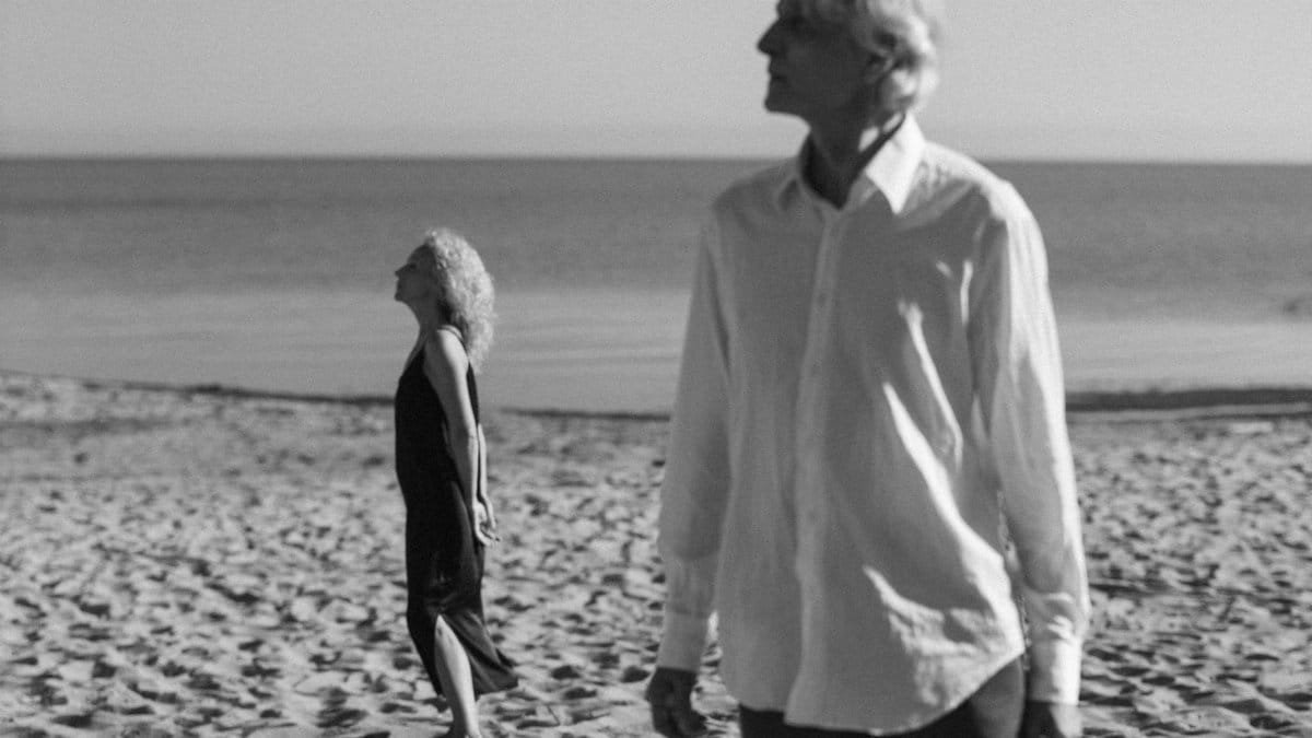 An elderly couple walking on a serene beach, captured in monochrome, embracing tranquility.