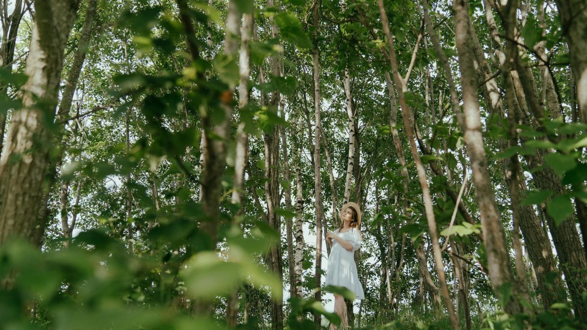 A woman in a straw hat and white dress enjoying a summer day in a serene forest setting.