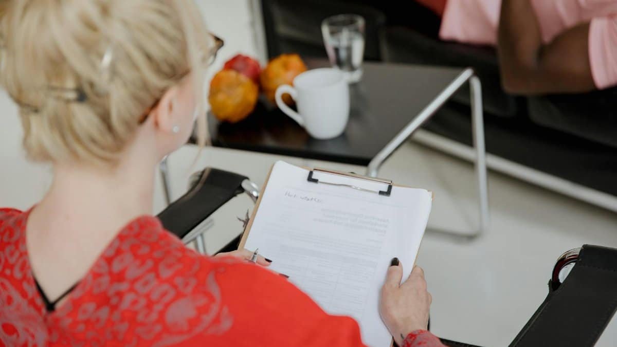 A psychologist takes notes during a therapy session with a client, indoors.