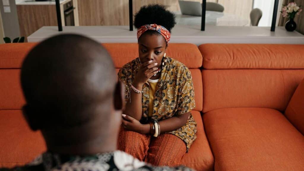 A thoughtful couple seated on a vibrant orange couch in a cozy living room setting.