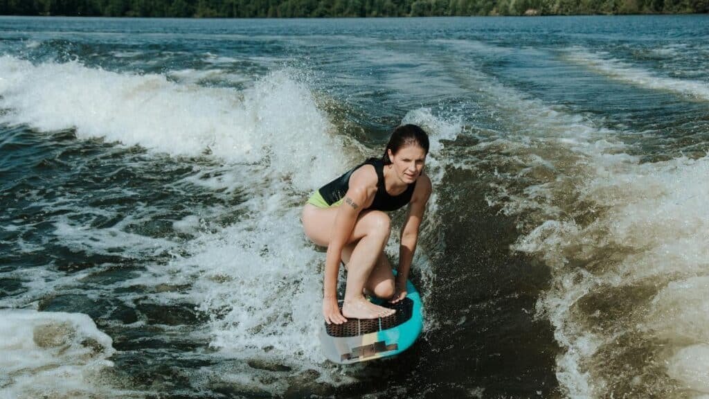 Woman crouching on a wakesurf board, surfing waves on a sunny day.