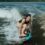 Woman crouching on a wakesurf board, surfing waves on a sunny day.