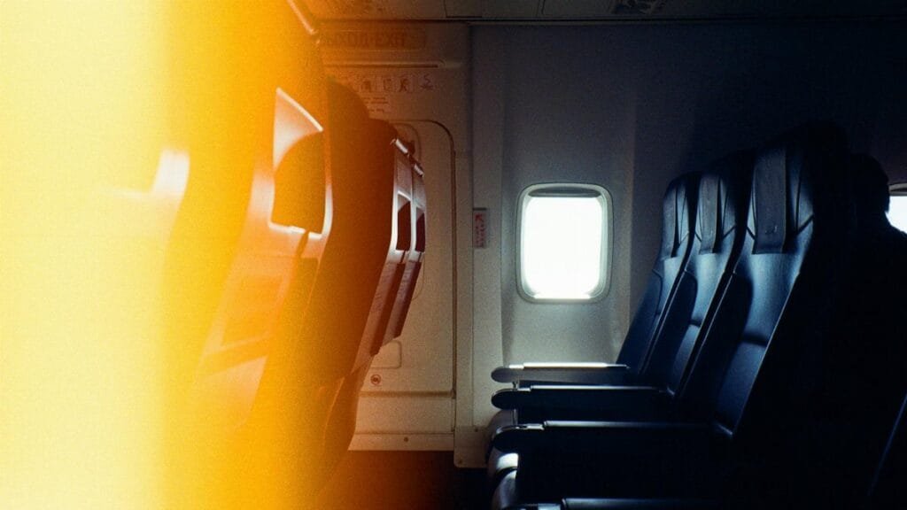 Interior view of empty airplane seats next to a window with warm lighting effect.