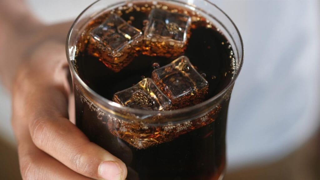 Close-up of a hand holding a glass of dark soda with ice cubes, creating a refreshing feel.