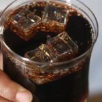 Close-up of a hand holding a glass of dark soda with ice cubes, creating a refreshing feel.