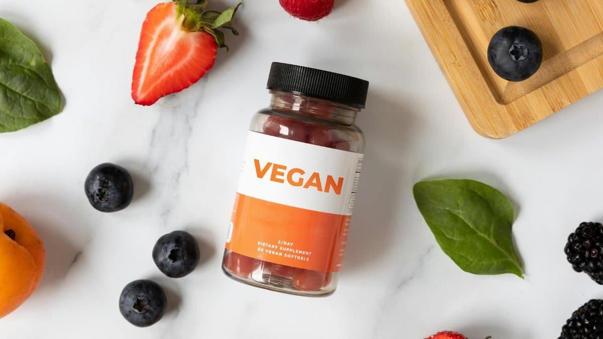 A flat lay of vegan supplements surrounded by fresh fruits on a white marble surface.