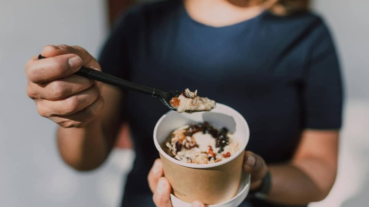Close-up of a person holding a bowl of vegan oatmeal topped with fruits.