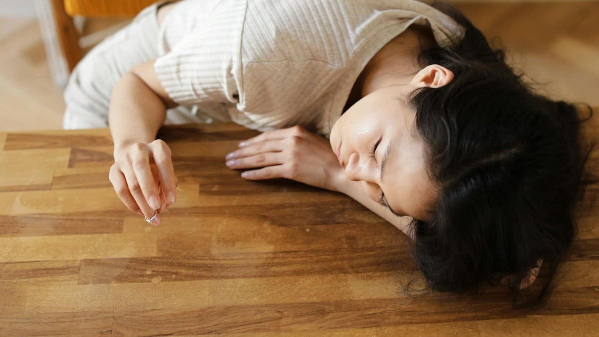 A woman lying sadly at a wooden table, holding a wedding ring, conveying emotions of separation and loss.