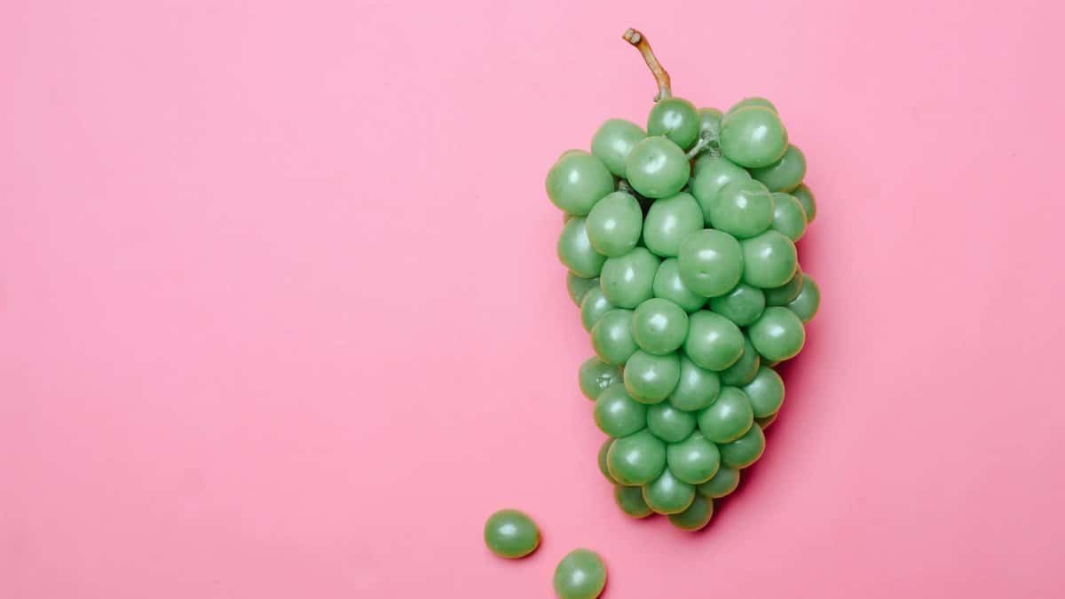 A bunch of vibrant green grapes on a pastel pink surface, perfect for healthy lifestyle themes.