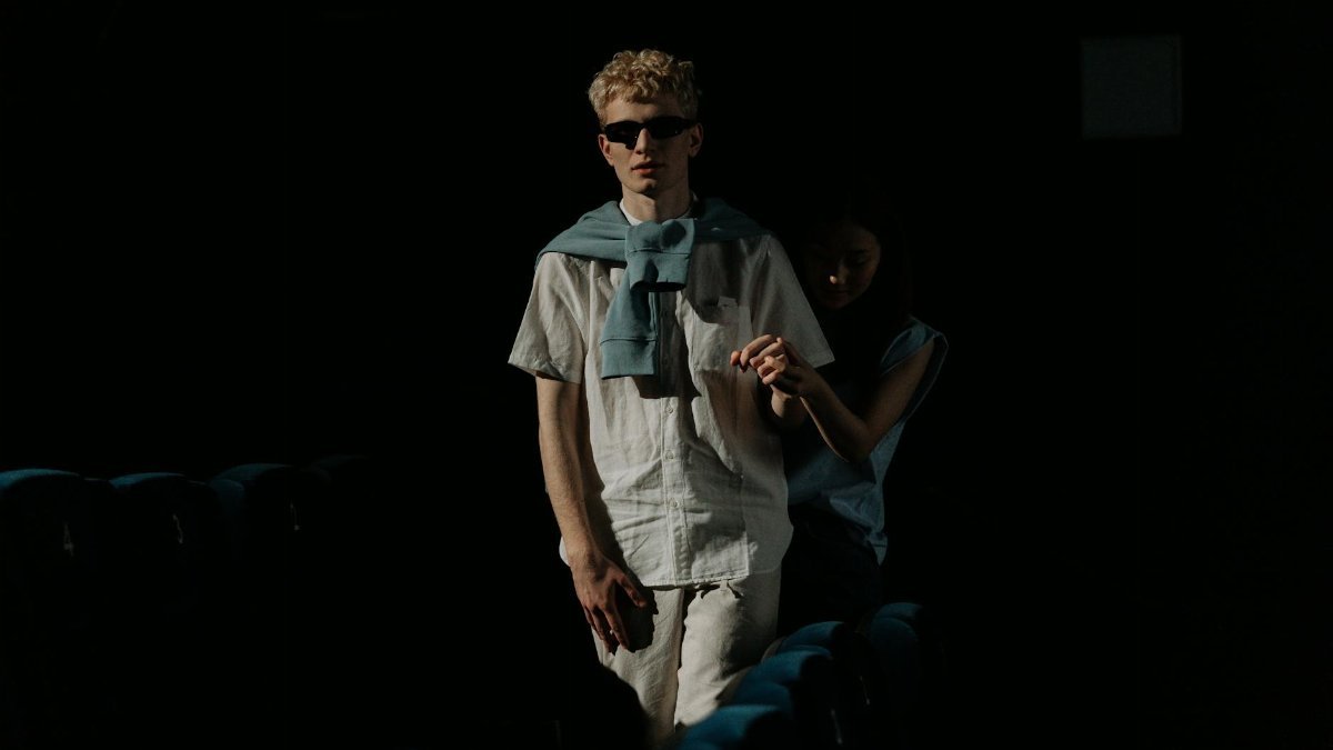 A visually impaired man with guide navigating through a dark movie theater.