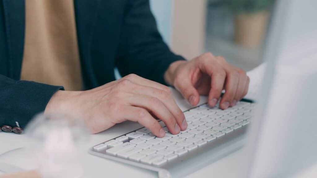 Close-up of hands typing on a white keyboard in an office setting. Ideal for business or technology themes.