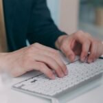 Close-up of hands typing on a white keyboard in an office setting. Ideal for business or technology themes.