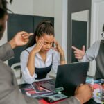 Two colleagues stress a coworker during an intense team meeting in a modern office setting.