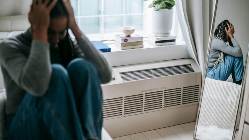 Frustrated young female having mental problem reflecting in mirror while sitting alone in room