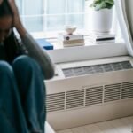 Frustrated young female having mental problem reflecting in mirror while sitting alone in room