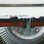 Close-up of a vintage typewriter with the quote '...and so it begins'.