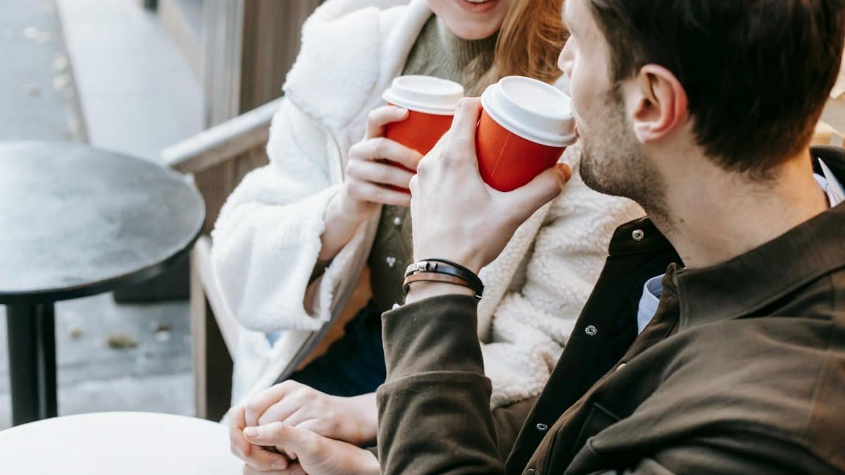 A couple enjoying a warm drink and holding hands during an outdoor autumn date.