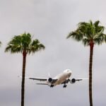 Airplane landing at Los Angeles International Airport surrounded by palm trees under cloudy skies.