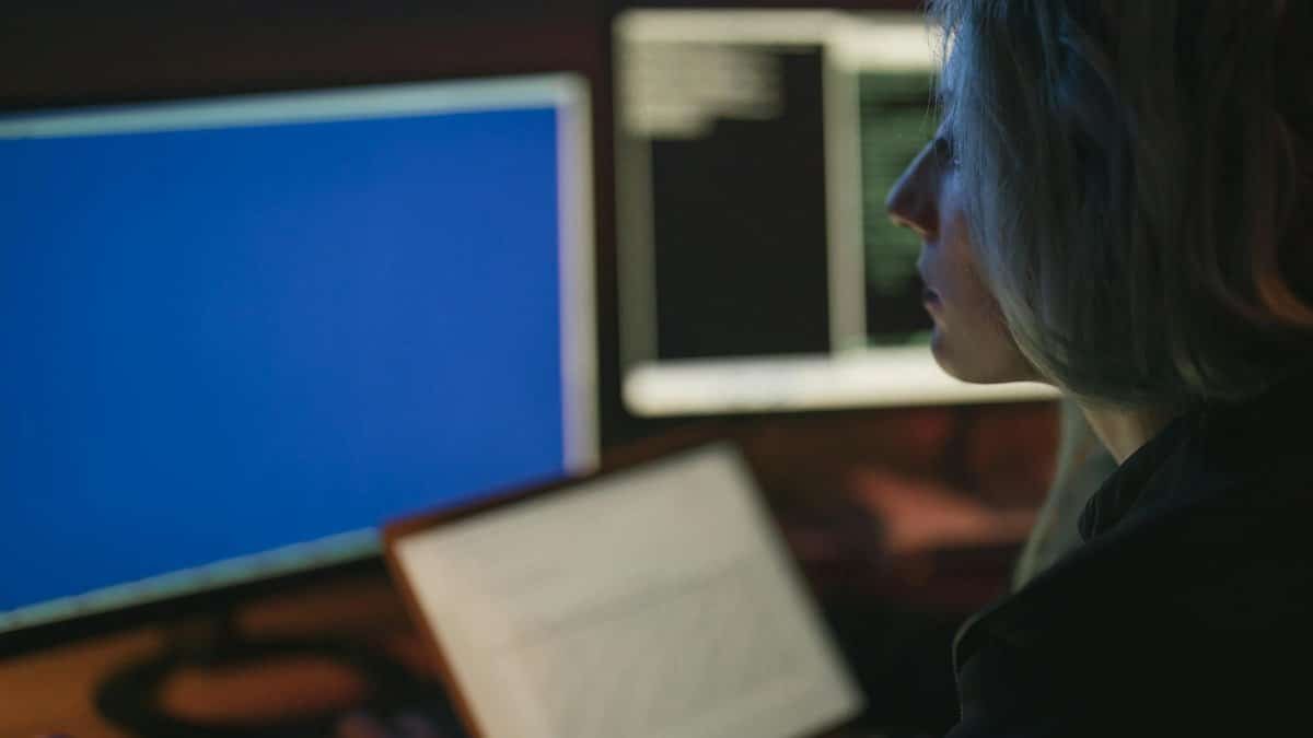 A woman working on multiple computer screens at night, focusing on her tasks.