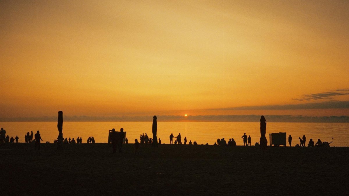 Silhouetted people on a beach enjoying a serene sunset over calm waters.